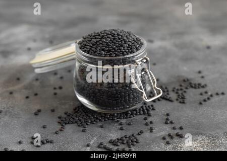 Vaso di vetro di fagioli di lenticchie nere asciutti su tavola grigia da vicino. Alimentazione sana, fonte di proteine per vegan e dieta vegetariana. Tradizionale Asiatico e Nort Foto Stock