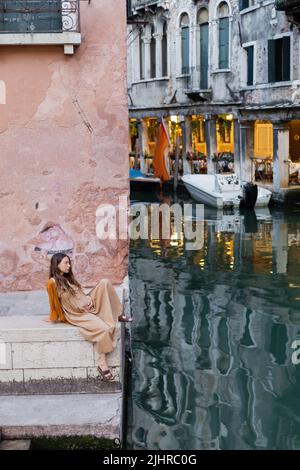 Vista laterale della giovane donna incinta seduta sulle scale dell'edificio di Venezia Foto Stock