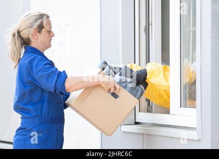 Nordhorn, Germania. 20th luglio 2022. Un dipendente dell'ufficio veterinario della contea fornisce abbigliamento usato a una struttura di decontaminazione per la pulizia. In precedenza, era in un'azienda agricola, che si trova in una zona di sorveglianza. Dopo l'epidemia di peste suina africana in un'azienda agricola dell'Emsland meridionale, le contee colpite stanno adottando ulteriori misure per controllare la malattia animale. Un centro di logistica comune per le malattie animali ha iniziato le operazioni nelle contee di Grafschaft Bentheim e Emsland a Nordhorn. Credit: Friso Gentsch/dpa/Alamy Live News Foto Stock