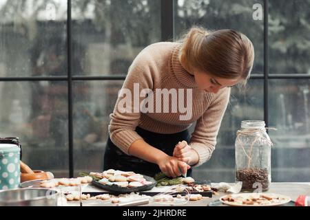 Giovane donna che decora la pasticceria in cucina Foto Stock