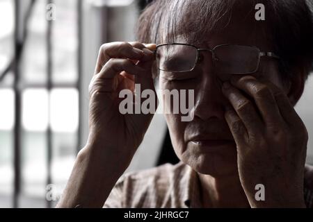 Immagine parziale della silhouette dell'anziano asiatico che gli sfrega l'occhio. Concetto di dolore oculare, sforzo o prurito palpebrale. Foto Stock