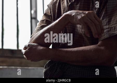 Immagine parziale della silhouette del dolore nel gomito dell'anziano del sud-est asiatico. Concetto di dolore al gomito o osteoartrite. Foto Stock