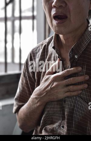 L'anziano asiatico soffre di senso di costrizione toracica. Può essere causato da asma, bronchite, bronchiolite, polmonite, infarto miocardico, h ischemica Foto Stock