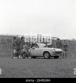 1974, storico, manager di calcio, Malcolm Allison seduto in 2 porte Vauxhall Chevette hatchback auto sul campo al Selhurst Park, con i giocatori di squadra in piedi intorno. Selhurst Park è la sede del Crystal Palace Football Club. In cima alle terrazze, una bancarella di cibo, Dogs & Onions. Foto Stock