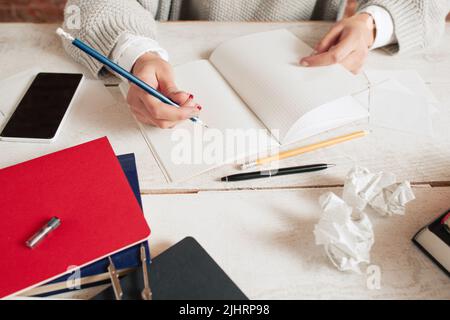 Donna che scrive in notebook su un ambiente di lavoro disordinato Foto Stock