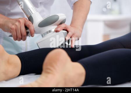 Il beautician fa il massaggio di vitello di LPG delle gambe alla donna giovane in vestito nero. Massaggio linfodrenante. Trattamenti dimagranti Foto Stock