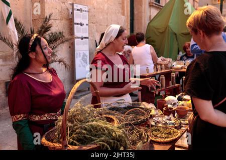 Due Signore una vestita da erborista che spiega l'uso delle erbe ad uno spettatore, l'altra vestita da donna ricca. Mdina festa medievale, Malta Foto Stock