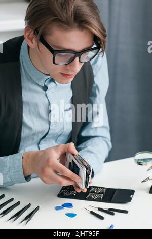 Uomo che dismonta lo smartphone in officina Foto Stock