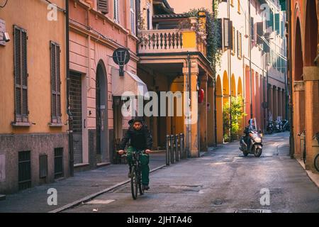 Un ciclista che percorre una stradina stretta con edifici colorati a Bologna, in Italia di giorno Foto Stock