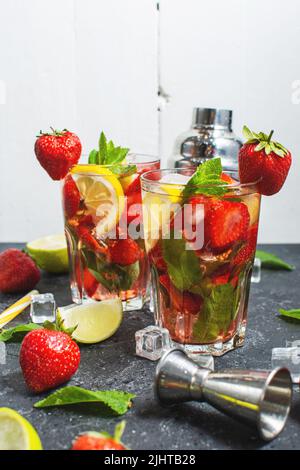 Cocktail mojito estivo rinfrescante con fragola, menta e lime con shaker per montare le bevande su un tavolo di pietra scura Foto Stock