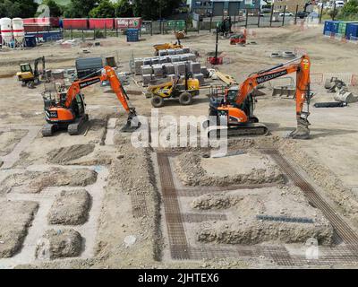 Pontypridd, Galles - Luglio 2022: Doghe meccaniche parcheggiate accanto alle fondamenta di nuove case in costruzione su un campo marrone sviluppo. Foto Stock