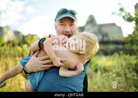 Carino ragazzo toddler fra le braccia dei padri. Papà e figlio che si divertono nella soleggiata giornata estiva della città. Adorabile bambino tenuto dal suo papà. Foto Stock