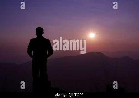 Una silhouette di un giovane maschio su sfondo viola al tramonto Foto Stock