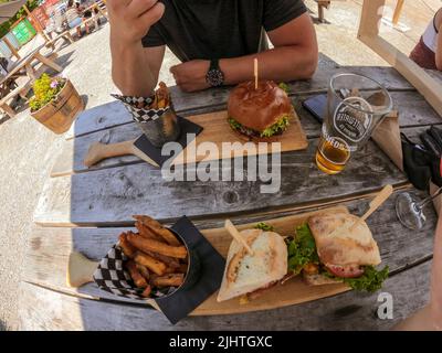Punto di vista dei giovani amici che mangiano hamburger, sandwich nel patio del ristorante dopo il lavoro - concetto di amicizia con persone felici che godono di tempo insieme Foto Stock