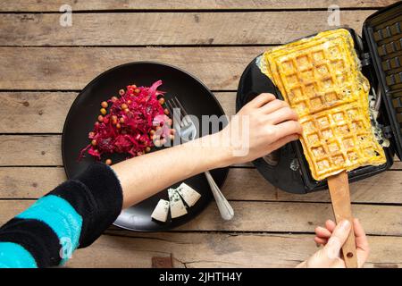 friggete le uova strapazzate con formaggio e spezie in un ferro da stiro per waffle su un tavolo di legno in cucina, fate bollire le uova strapazzate in un ferro da stiro per waffle, colazione Foto Stock