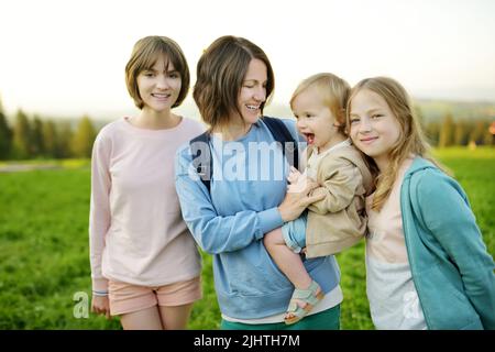 La giovane madre e i suoi tre bambini si divertono all'aperto nella giornata estiva soleggiata. I bambini esplorano la natura. Alte montagne e verdi colline in estate o in primavera Foto Stock