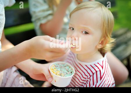 Sorella grande che allatta gustose gocce di gelato al fratello del bambino. Dolci per bambini. Foto Stock