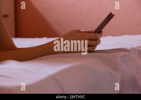 una ragazza tiene un telefono nelle sue mani sul letto di notte nella camera da letto, la comunicazione al telefono mentre dorme di notte sul letto, un telefono nel suo ha Foto Stock