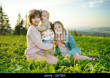 Due sorelle e il loro fratello minore si divertono all'aperto nella giornata estiva soleggiata. I bambini esplorano la natura. Alte montagne e verdi colline in estate o. Foto Stock