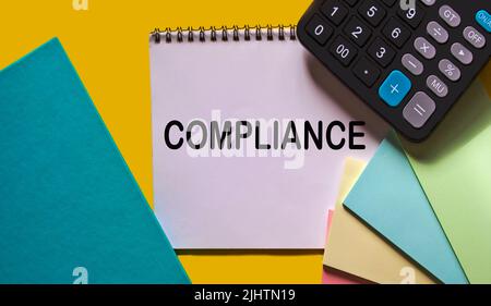 WORD COMPLIANCE su blocco note con calcolatrice, blocco note e adesivi su sfondo giallo Foto Stock