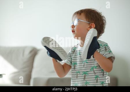 Bambino con autismo in occhiali giocare con le sue scarpe Foto Stock