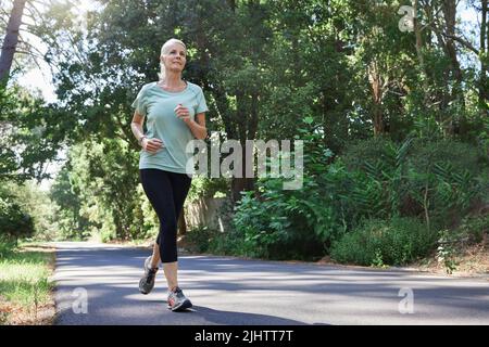 Non è mai troppo tardi per correre. Inquadratura a basso angolo di una donna matura che corre all'aperto. Foto Stock