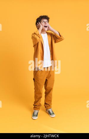 Vestito bianco da ragazzo che esprime sorpresa e guarda verso l'alto isolato su sfondo giallo Foto Stock