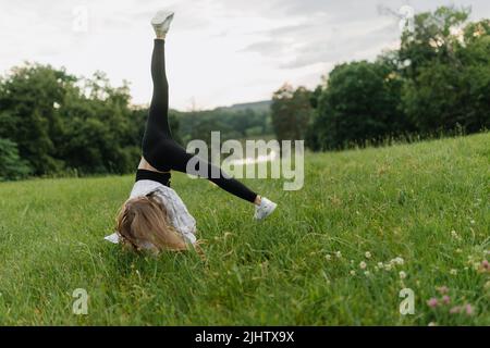 Una ragazza con leggings neri e una T-shirt bianca sta facendo un cartwheel sull'erba Foto Stock