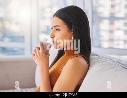Ma prima di tutto, mi permetta di godere il mio frullato. Una donna che beve un frullato mentre si rilassa sul divano a casa. Foto Stock