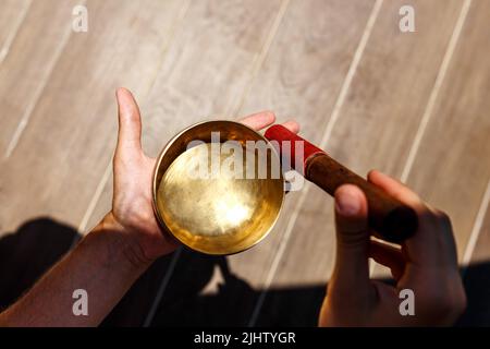 L'uomo mani usando la ciotola di canto nella terapia healing del suono all'aperto, primo piano. Foto Stock