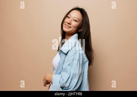 Bella goduto piuttosto abbronzato adorabile giovane signora asiatica sorridente alla macchina fotografica che posa isolata su sfondo beige pastello. Concetto di persone ed emozioni. Copia Foto Stock