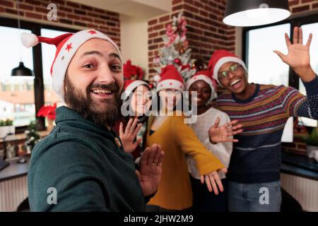 Gruppo vario di persone che scattano foto con albero di natale, festeggiando la stagione con le decorazioni di festa in ufficio di affari. Colleghi che scattano foto con ornamenti natalizi stagionali. Foto Stock