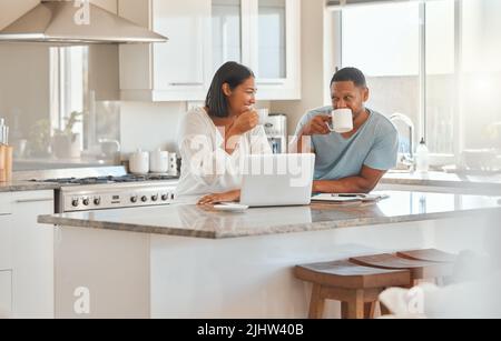Siete pronti per il tè. Una coppia beve il caffè mentre si usa un computer portatile in cucina a casa. Foto Stock