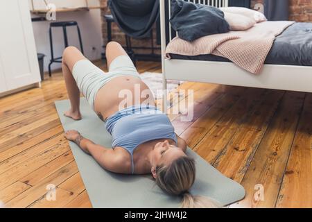 Allenamenti per donne in gravidanza. Camera da letto interna ripresa di una donna incinta caucasica che si esercita su un tappeto yoga. Mantenersi in forma durante la gravidanza. Foto di alta qualità Foto Stock