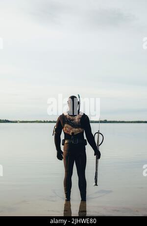 Uomo che tiene una pistola e in piedi in acqua di mare. Vista posteriore dell'uomo che indossa una muta che si prepara ad andare la pesca di spearfishing sotto l'acqua. Foto Stock