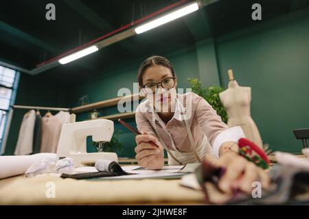 Designer femminile creativa che lavora nel suo studio di moda. Dressmaker asiatico che lavora su schizzi sul suo posto di lavoro e selezionare il panno. Foto Stock