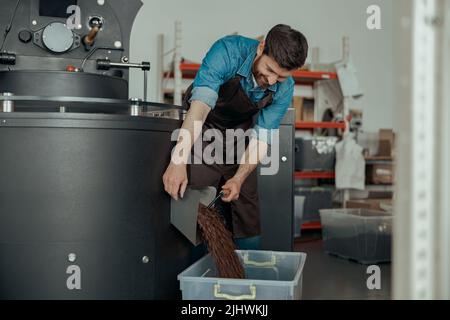 Il proprietario di affari che versa i fagioli di caffè torrefatti nella scatola speciale dalla macchina di tostatura per vendere Foto Stock