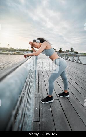 Mettendo il suo corpo attraverso la suoneria. Scatto a tutta lunghezza di una giovane atleta attraente che prende una pausa durante la sua corsa mattutina fuori. Foto Stock