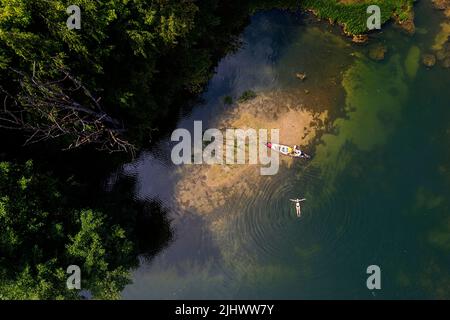 Veduta aerea di una donna che si rilassa mentre nuota vicino al banco di sabbia, donna in un viaggio in canoa su un bellissimo fiume Krka in Slovenia Foto Stock