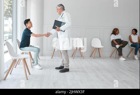 Un medico maturo che scuote le mani con un giovane nella sala d'attesa di una clinica. Foto Stock
