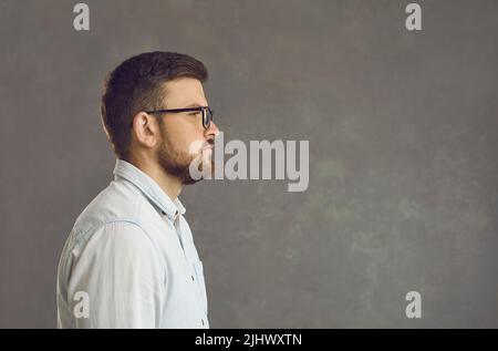 Ritratto laterale di giovane uomo serio sicuro in camicia su sfondo grigio Foto Stock
