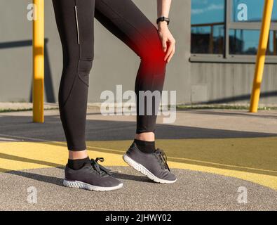 Dolore al ginocchio dell'atleta. Trauma sportivo causato da frattura rotulare, lussazione, lesione da legamenti. Donna che tiene una gamba dolorosa con punto rosso. Problema dei corridori. Concetto di assistenza sanitaria. Foto di alta qualità Foto Stock