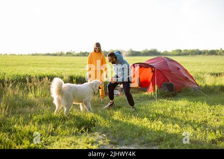 Le giovani coppie giocano con il loro cane al campeggio Foto Stock