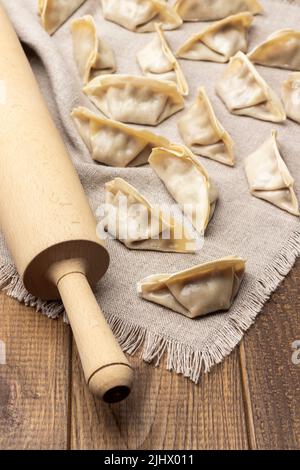 Rolling pin e gnocchi grezzi di gyoza su tovagliolo di lino. Vista dall'alto. Sfondo in legno Foto Stock