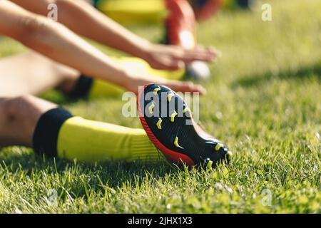 Il giocatore di calcio si allunga seduto sul campo di erba. Stretching sessione dopo allenamento per calciatori. Giocatore in calze e scarpe da calcio Foto Stock