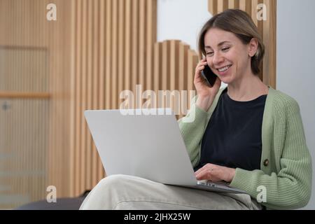 Felice donna d'affari di mezza età che utilizza un dispositivo mobile per le comunicazioni di lavoro mentre lavora online Foto Stock