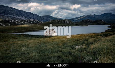 Il remoto altopiano Bothy seduta in solitudine sulle rive del Loch Stack.Wwith montagna cime di Arkle in background Foto Stock