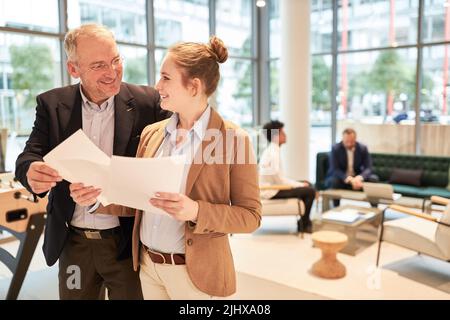 Responsabile o consulente di successo e giovane collega femminile con documenti aziendali in ufficio Foto Stock