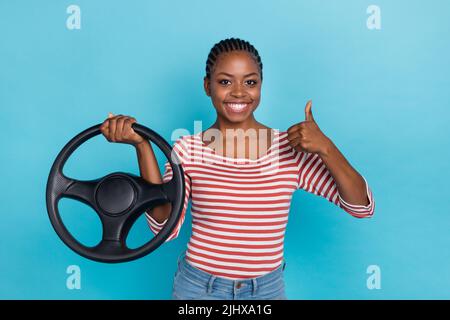 Ritratto di bella ragazza positiva mano tenere ruota dimostrare pollice su isolato su sfondo blu colore Foto Stock