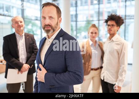 Uomo d'affari fiducioso come capo e manager con il suo team in background Foto Stock